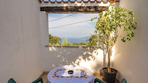 A small balcony with a round table and two chairs, a potted plant, and a view of the sea.