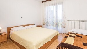 A bedroom with a bed, a nightstand, a radiator, and a window with sheer curtains.