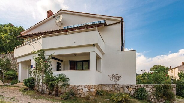 A two-story building with a flat roof, a satellite dish, and a stone foundation.