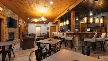 Un interior rústico con chimenea de piedra, techo de madera y zona de bar con luces colgantes.
