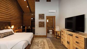 A log cabin-style bedroom with a large bed, wooden headboard, a flat-screen TV, and a wooden dresser.
