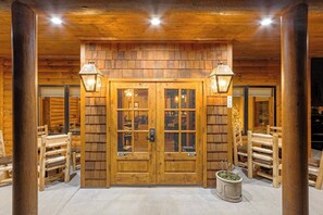 A log cabin entrance with a wooden door, two exterior lights, and a potted plant.