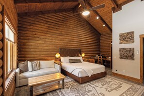 Un dormitorio tipo cabaña de madera con una cama, un sofá, un banco de madera y un tapete estampado.