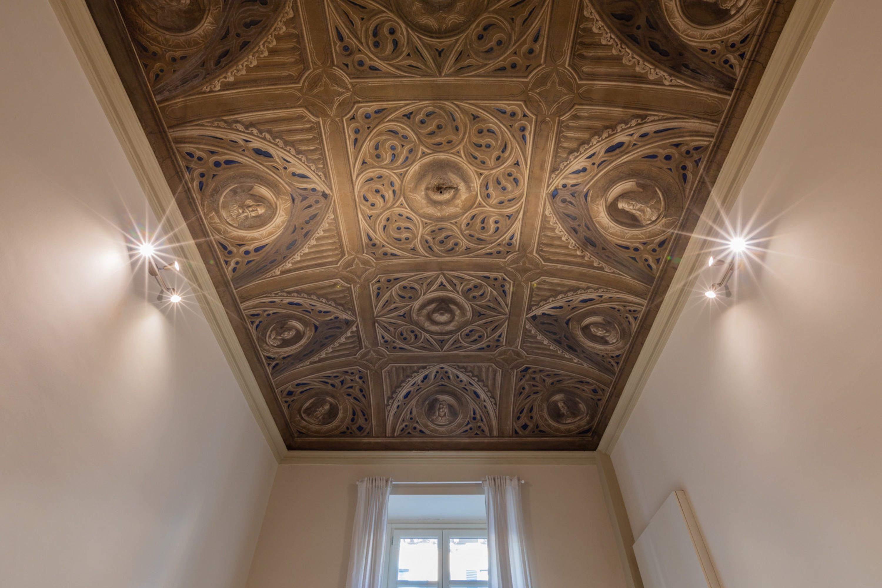A room with a decorative ceiling featuring intricate patterns and recessed lighting.