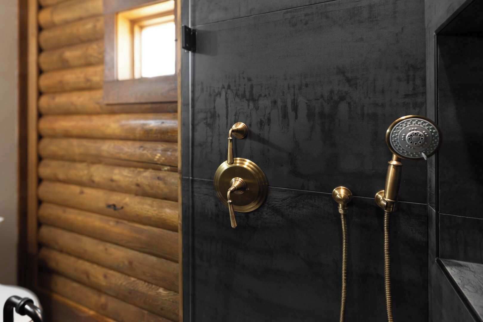Un baño con puerta negra, ducha de caño de latón y ventana con listones de madera.