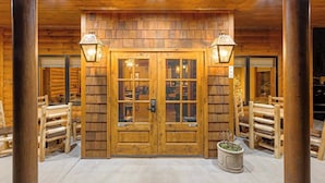 A wooden log cabin entrance with a double door, two wall-mounted lamps, and a potted plant.