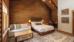 A log cabin bedroom with a bed, a sofa, a wooden bench, and two wall-mounted lamps.