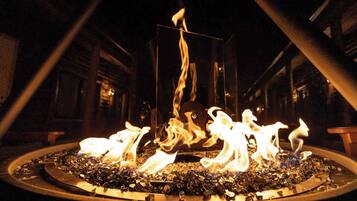 Un foyer dont les flammes s’élèvent dans un récipient métallique circulaire, le tout intégré dans un décor industriel sombre.
