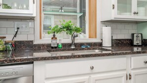 Une cuisine avec des meubles blancs, un plan de travail en granit, une fenêtre donnant sur un beau paysage et un égouttoir à vaisselle.