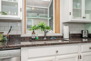 A kitchen with white cabinets, a granite countertop, a window with a view, and a dish rack.