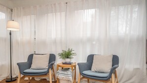 Une pièce avec deux fauteuils bleus, une petite table en bois sur laquelle est posée une plante, et un lampadaire.