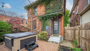 A backyard with a hot tub, a brick house with ivy, and a wooden fence.