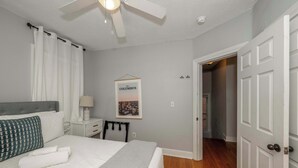A bedroom with a bed, a nightstand, a framed picture on the wall, and a door leading to another room.