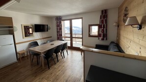 A modern kitchen with a built-in refrigerator, a dining area with a wooden table and chairs, a sofa, and a balcony with a view of the mountains. - VALMEINIER : Beautiful apartment in the heart of Valmeinier 1900, 8 people (Valmeinier)