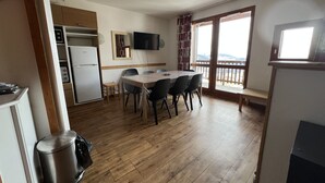 A compact kitchen with a refrigerator, stove, and sink. There is a dining table with chairs and a television mounted on the wall. - VALMEINIER : Beautiful apartment in the heart of Valmeinier 1900, 8 people (Valmeinier)