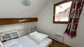 A bedroom with a wooden headboard, a bed with white bedding, a bedside table, and a window with curtains. - VALMEINIER : Beautiful apartment in the heart of Valmeinier 1900, 8 people (Valmeinier)