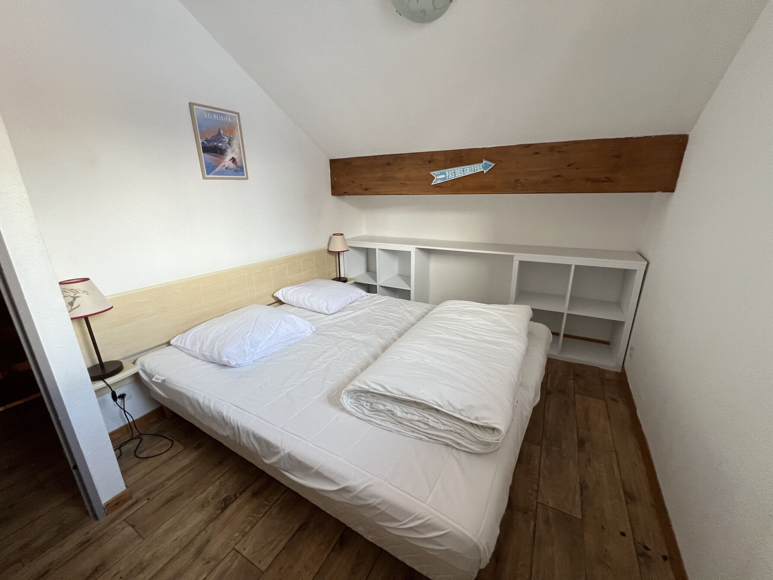 Une chambre à coucher comprenant un lit, une table de chevet, une lampe, une tête de lit en bois et une étagère fixée au mur.