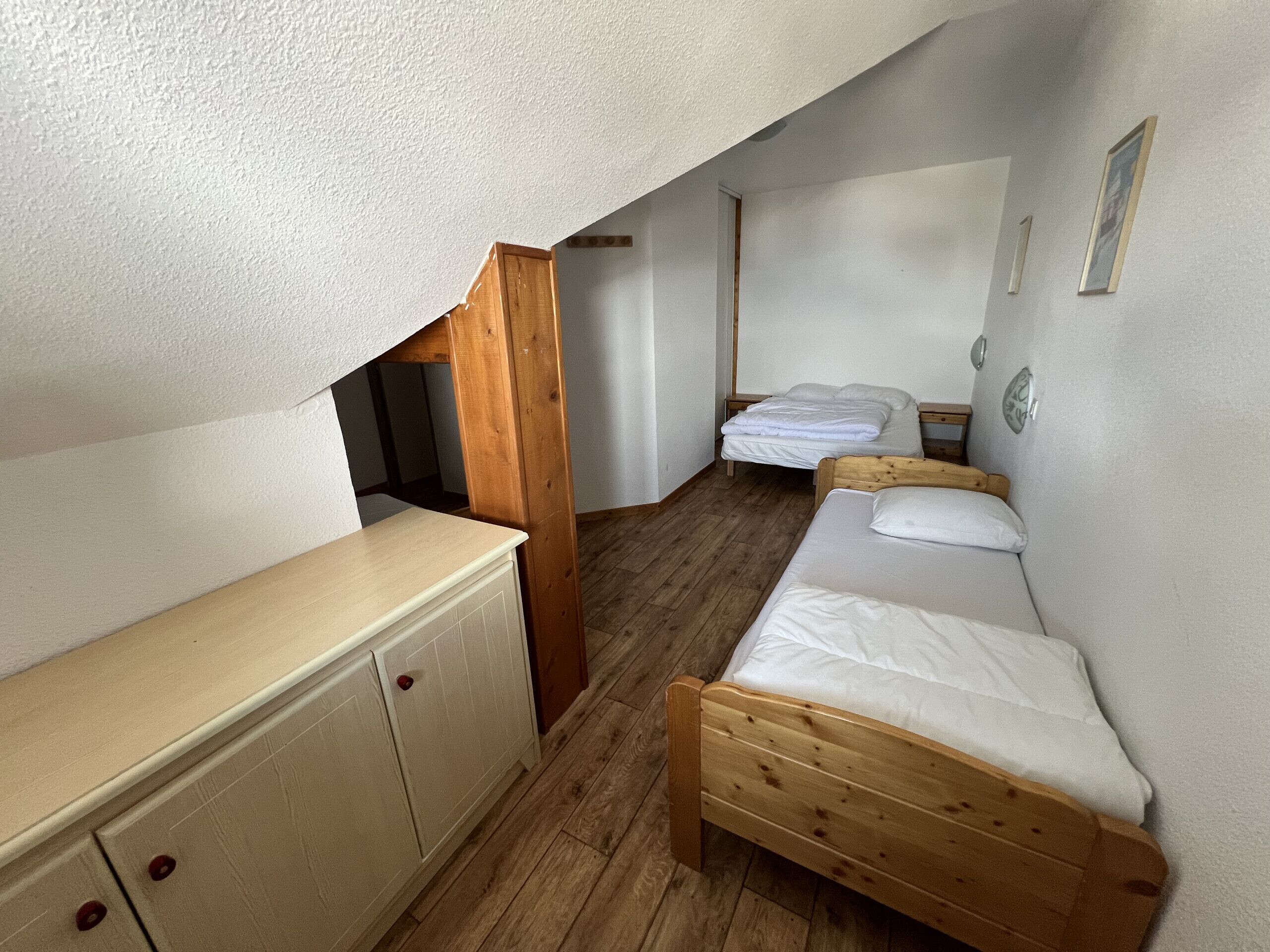 Une petite pièce, de taille modeste, avec deux lits en bois, une commode en bois et un plafond en pente.