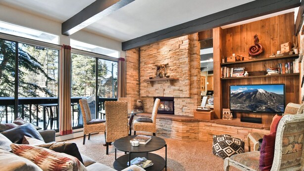 A cozy living room with a stone fireplace, comfortable seating, and a large TV. - Tamarisk Après Condo: Walk to Slopes/Town (Breckenridge)