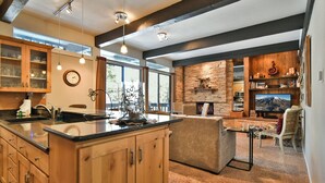A modern kitchen with wooden cabinets, a central island, and a stone accent wall. - Tamarisk Après Condo: Walk to Slopes/Town (Breckenridge)