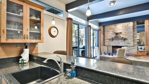 A kitchen with granite countertops, a stainless steel sink, wooden cabinets, and a stone fireplace. - Tamarisk Après Condo: Walk to Slopes/Town (Breckenridge)