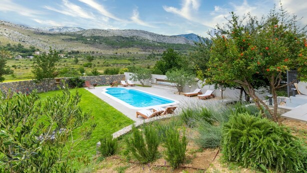 A swimming pool surrounded by a well-maintained garden with a view of mountains in the background. - Serene Rural Villa With Pool, Sun Deck, and Children's Play Area (Omis)