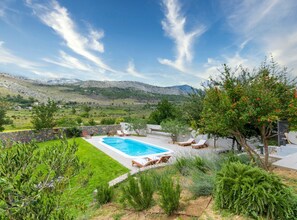 A swimming pool surrounded by a well-maintained garden with a view of mountains in the background. - Serene Rural Villa With Pool, Sun Deck, and Children's Play Area (Omis)