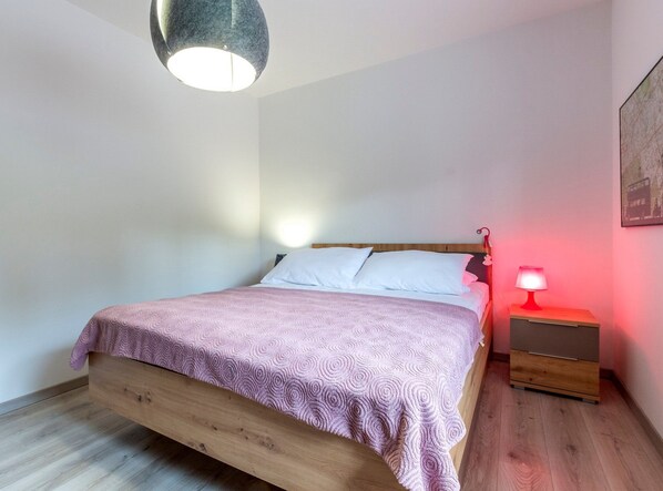 A bedroom with a wooden bed, a bedside table with a lamp, and a painting on the wall. - Serene Rural Villa With Pool, Sun Deck, and Children's Play Area (Omis)