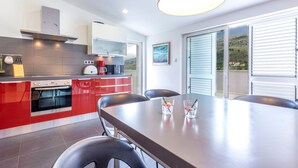 A modern kitchen with red cabinets, a built-in oven, and a dining area with a table and chairs. - Serene Rural Villa With Pool, Sun Deck, and Children's Play Area (Omis)
