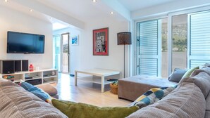 A modern living room with a flat-screen TV, a sofa set, a coffee table, and a large window with blinds. - Serene Rural Villa With Pool, Sun Deck, and Children's Play Area (Omis)