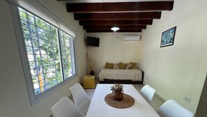 Un comedor con una mesa blanca, sillas blancas, un mantel tejido y un jarrón con plantas secas.