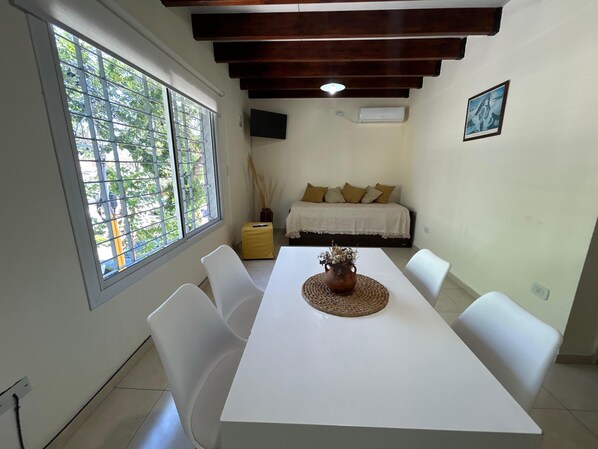 A dining area with a white table, white chairs, a woven placemat, and a vase with dried plants.