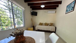 Una habitación con cama, televisor montado en la pared y ventana con vista a follaje.