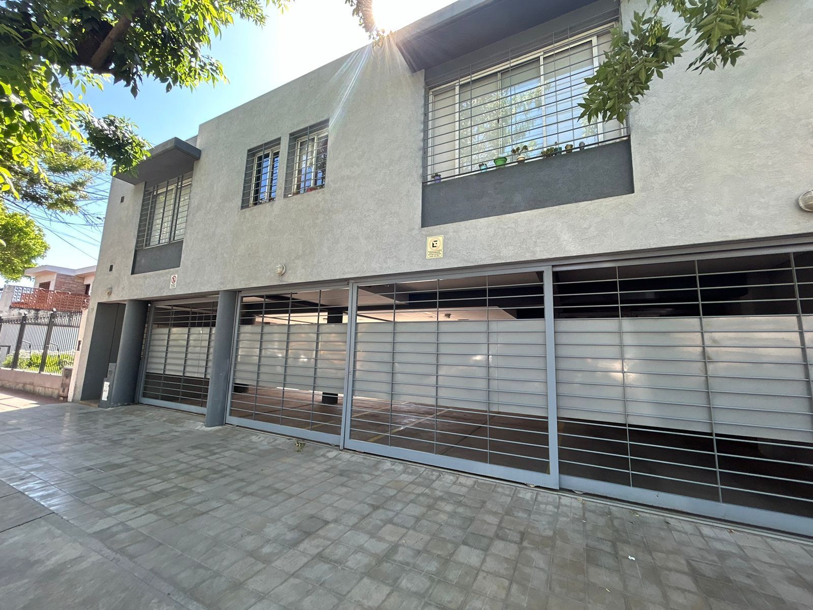 Un edificio moderno con una puerta de garaje, un ventanal con un letrero y una acera pavimentada.