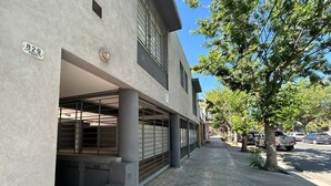 Un edificio con acceso a garaje, medidor de gas y una calle con coches estacionados y árboles.