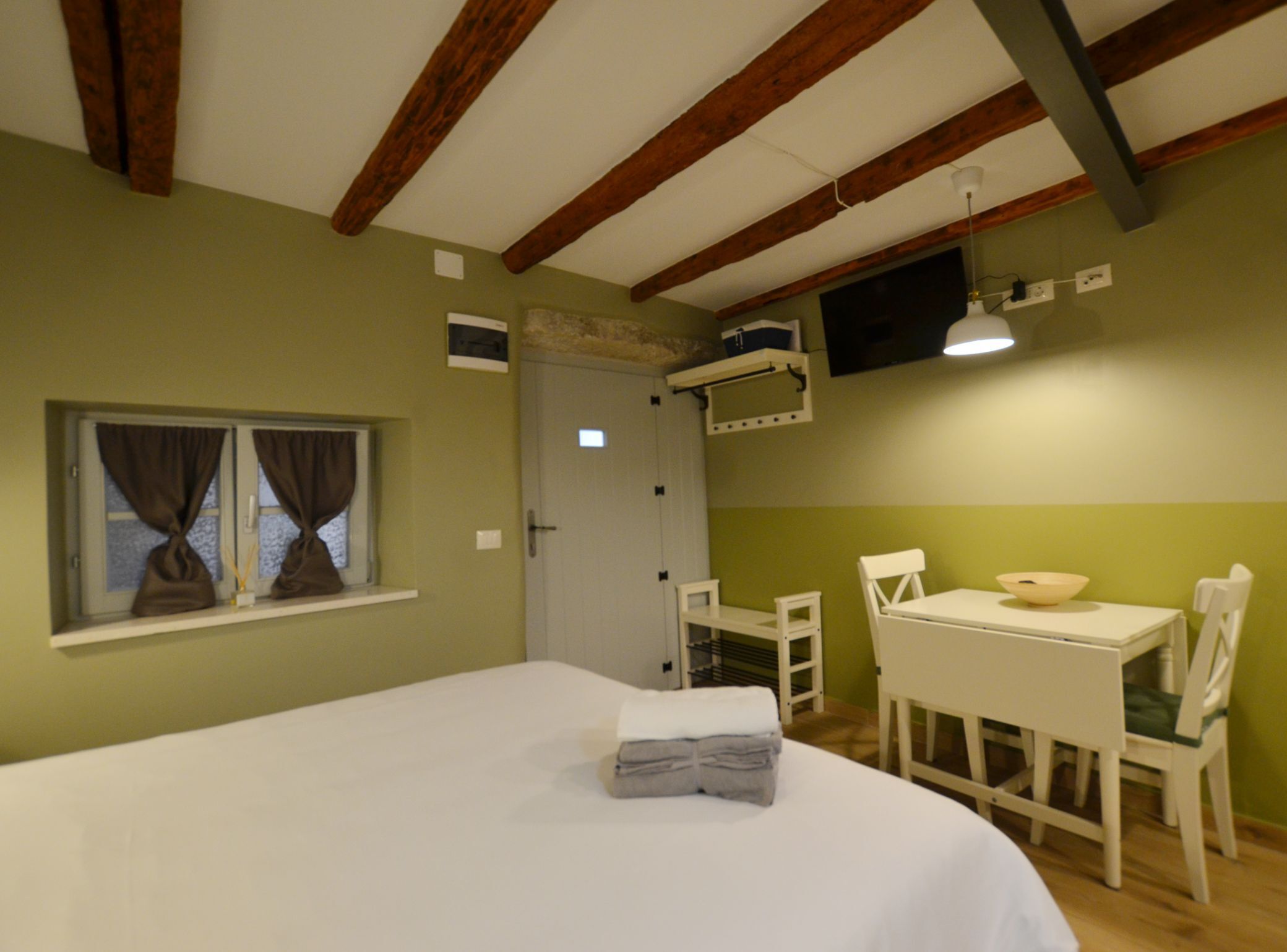 Een kamer met een bed, een tafeltje met stoelen, een raam met gordijnen en een deur.