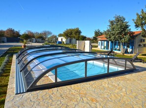 A swimming pool with a glass enclosure, stone flooring, and a view of a residential area with houses and trees. - Golden and Green Acres Holiday Home With Pool and Sauna (Rovinj)