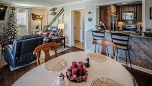 Ein gemütliches Wohnzimmer mit Kamin, eine Essecke mit Tisch für vier Personen und eine Küche mit Holzausstattung und modernen Geräten.