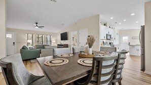 A spacious living room with a dark wooden dining table, grey upholstered sofas, and a kitchen in the background. - The Oak Hideaway | Pet Friendly 3Bd! (St. Augustine)