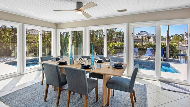 A dining area with a wooden table, grey chairs, and a ceiling fan. - Siesta Dreamin’ - Canal Front Home with Private Pool and Dock! (Siesta Key)