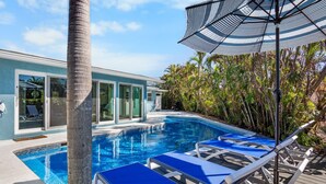 A pool area with blue lounge chairs and a striped umbrella. - Siesta Dreamin’ - Canal Front Home with Private Pool and Dock! (Siesta Key)