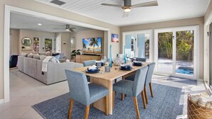A spacious living area with a dining table set for four, a sofa, and a view of a swimming pool. - Siesta Dreamin’ - Canal Front Home with Private Pool and Dock! (Siesta Key)