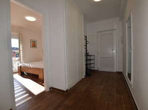 A hallway with a wooden floor, a bed in the left room, and a door at the end.