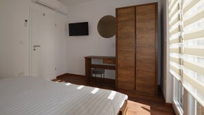 Un dormitorio con una cama, un escritorio, un armario, un televisor y una ventana con persianas.
