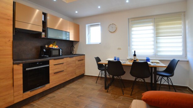 Una cocina moderna con armarios de madera, un microondas y un lavabo. Hay una mesa de comedor con sillas y una ventana con persianas.