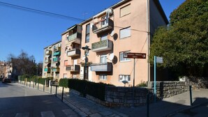 Un edificio residencial de varios pisos con balcones, vista a la calle y cielo despejado.
