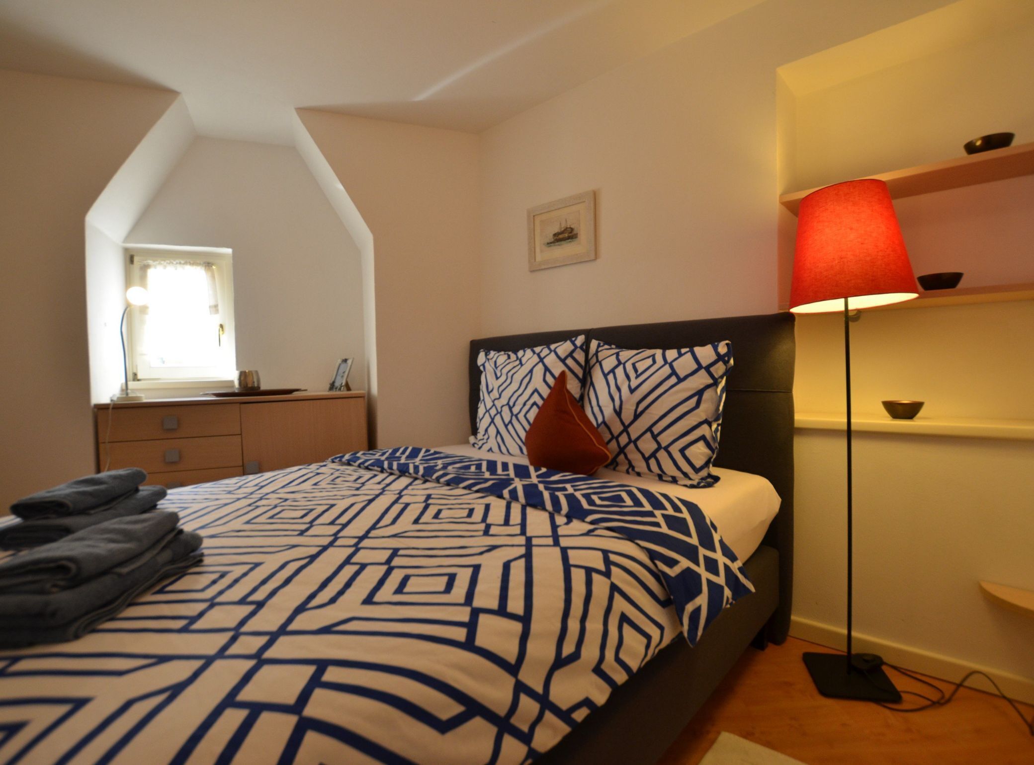 A bedroom with a bed, a nightstand, a lamp, and a window.