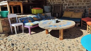 Un espace extérieur aménagé dans un style rustique, avec une table ronde en bois, un canapé agrémenté de coussins à motifs et un sol en pierre.