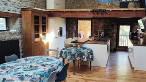 Une cuisine chaleureuse avec des poutres en bois, un coin repas avec des nappes à motifs floraux et un mur en pierre.