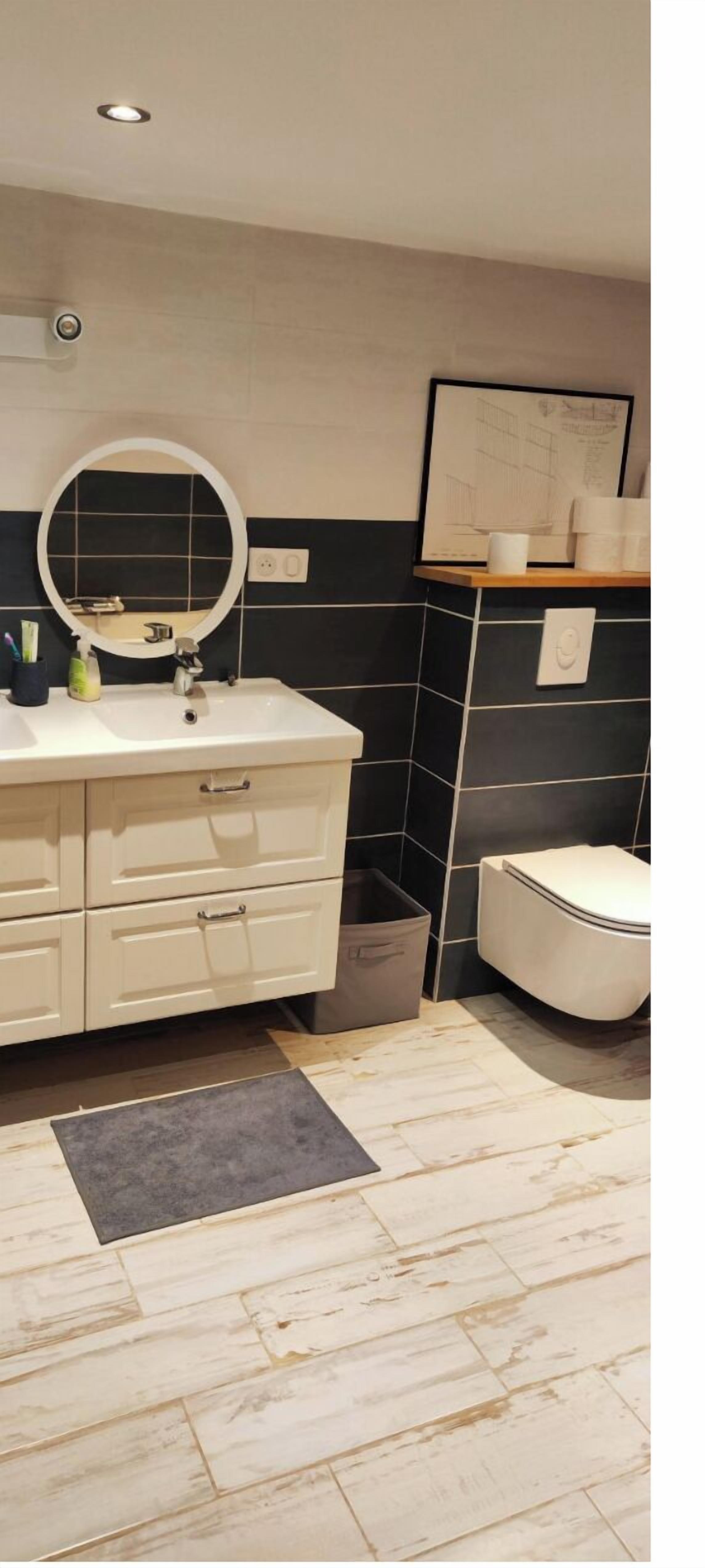 Een badkamer met een witte wastafel, een ronde spiegel, een toilet en een betegelde spatwand.